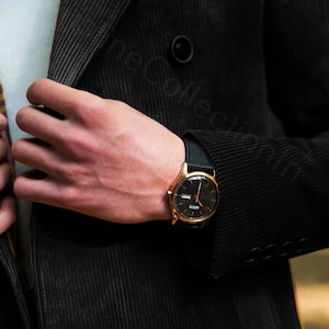 May include: A gold-toned wristwatch with a black leather band and a black face. The watch has a date window and a small second hand.