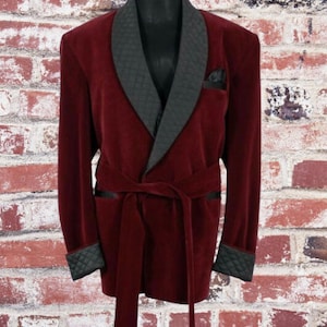 May include: A burgundy velvet robe with a black satin shawl collar and matching cuffs. The robe has a sash tie and tassel accents.