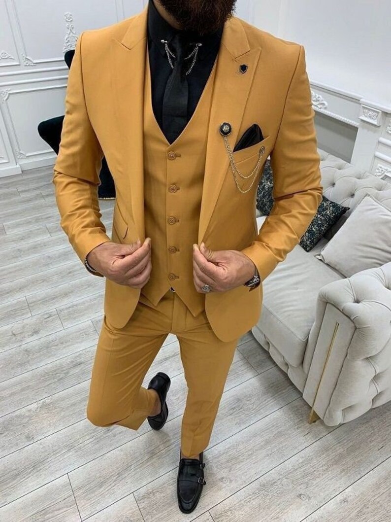 May include: A mustard yellow three-piece suit with a black button-down shirt and a black tie. The suit has a waistcoat with a chain and a pocket square.