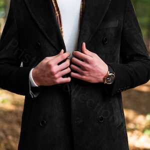 May include: A black corduroy double-breasted coat with a brown and yellow patterned scarf. The coat has two buttons on the front and a pocket on the left side.
