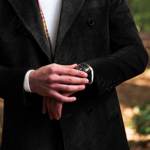 May include: A black corduroy double-breasted jacket with a gold watch on the left wrist.