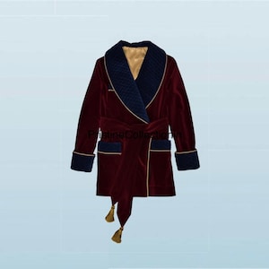 May include: A burgundy velvet smoking jacket featuring a quilted navy blue shawl collar and matching quilted cuffs. The jacket includes a tie belt with gold tassels, gold piping trim, and a smooth gold-colored interior lining.