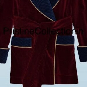 May include: A deep burgundy velvet robe featuring navy blue quilted lapels, cuffs, and pocket accents with gold piping trim. The garment includes a matching tie belt and the text PristineCollection in black lettering across the center front.