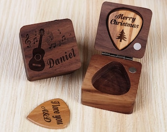 May include: A wooden box with a guitar and music notes engraved on the lid. The box is open and contains a guitar pick with the words "Merry Christmas" engraved on it. There is another guitar pick with the words "I love you A&D" engraved on it, lying on a wooden surface.