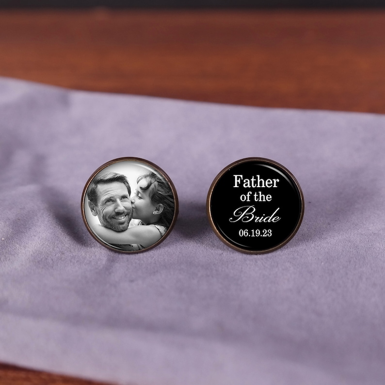 May include: A pair of cufflinks, one with a black background and the text "Father of the Bride 06.19.23" and the other with a photo of a man and a girl.