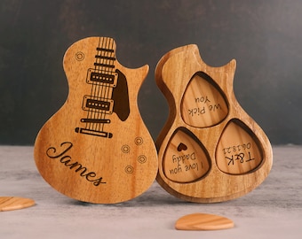 May include: Wooden guitar-shaped box with a guitar design and the name "James" engraved on the front. The box has three compartments for guitar picks, with the words "We Pick You", "I Love You Daddy", and "TR8K 06'18'21" engraved on the picks.