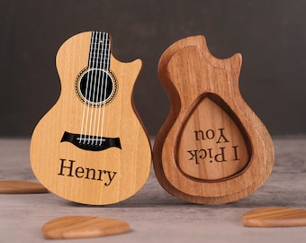 May include: A wooden guitar-shaped box with the name "Henry" engraved on the front. The box is open and reveals a smaller wooden box with the text "I Pick You" engraved inside. The boxes are on a brown surface.