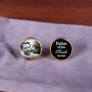 May include: Gold cufflinks with a black background. One cufflink features a photo of a man and a girl. The other cufflink has the text "Father of the Bride" and the date "06.19.23".