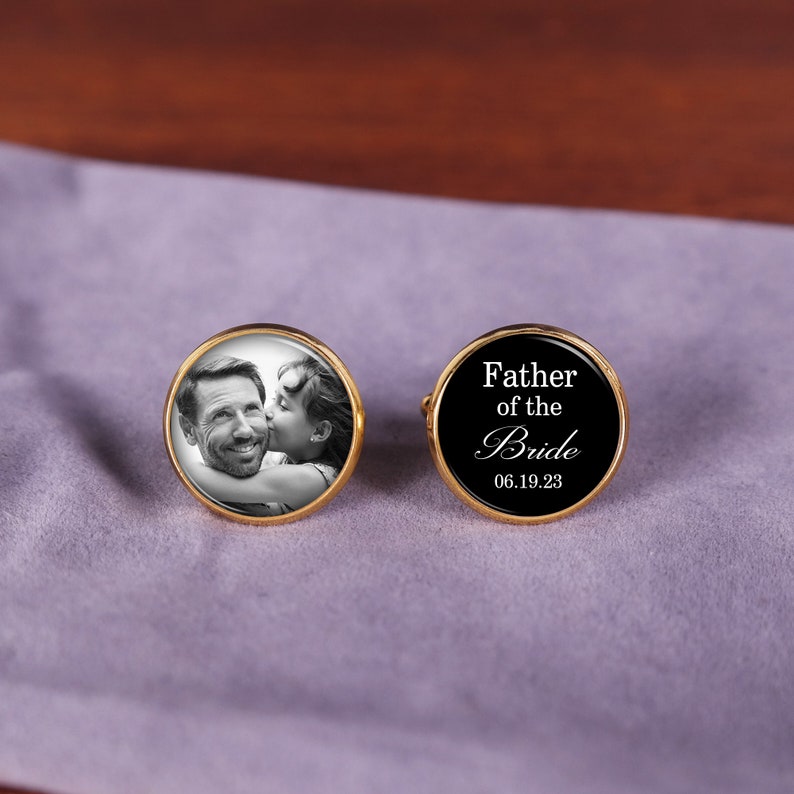 May include: Gold cufflinks with a black background. One cufflink features a photo of a man and a girl. The other cufflink has the text "Father of the Bride" and the date "06.19.23".