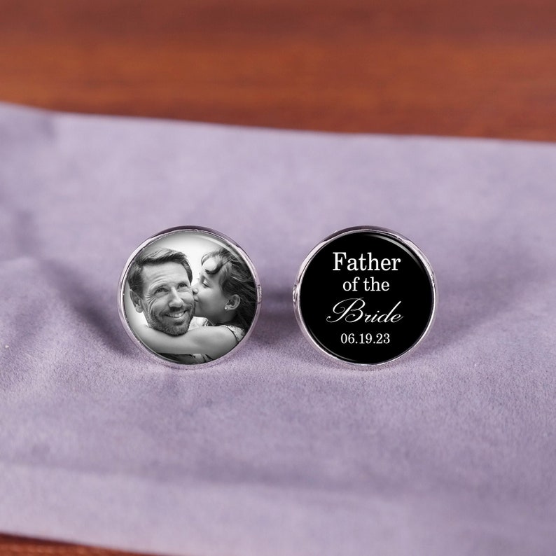 May include: A pair of cufflinks, one with a black background and the text "Father of the Bride" and the date "06.19.23", and the other with a black and white photo of a father and daughter.