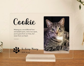 May include: A clear acrylic photo frame with a black paw print and heart design. The frame has a photo of a tabby cat and the text "Cookie Missing you unconditional love and playful paws, we're now apart, you're gone from our lives, but never from our heart. In Loving Memory 2014-2022".