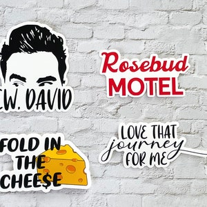 May include: Four white stickers with black text on a white brick wall. The stickers feature a black and white illustration of a man's face, the text "EW. DAVID", the text "FOLD IN THE CHEESE" with a cartoon wedge of cheese, the text "LOVE THAT journey FOR ME", and the text "Rosebud MOTEL".