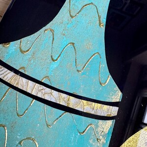 Puede incluir: Un jarr&oacute;n azul turquesa con una franja dorada y blanca y l&iacute;neas onduladas doradas en la superficie.