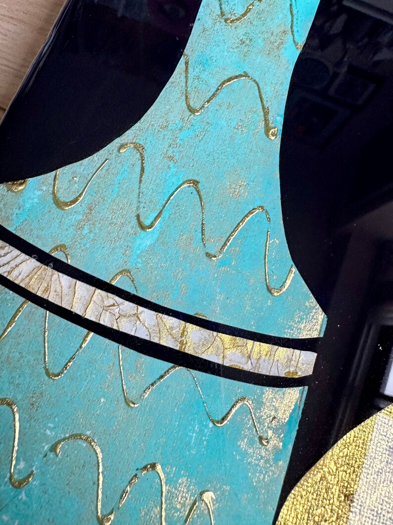 Puede incluir: Un jarr&oacute;n azul turquesa con una franja dorada y blanca y l&iacute;neas onduladas doradas en la superficie.