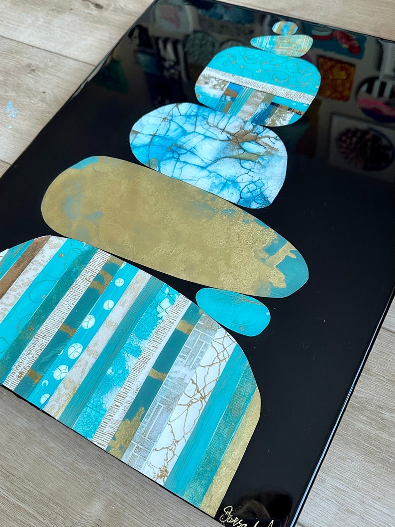 Puede incluir: Pintura abstracta de piedras apiladas en tonos de azul, dorado y blanco sobre un fondo negro.