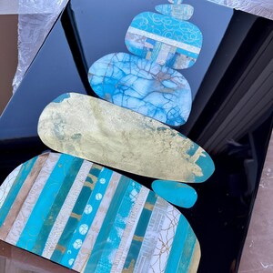 Puede incluir: Una pila de piedras abstractas de forma org&aacute;nica en tonos de azul, blanco y dorado, dispuestas en una formaci&oacute;n zen sobre un fondo negro.