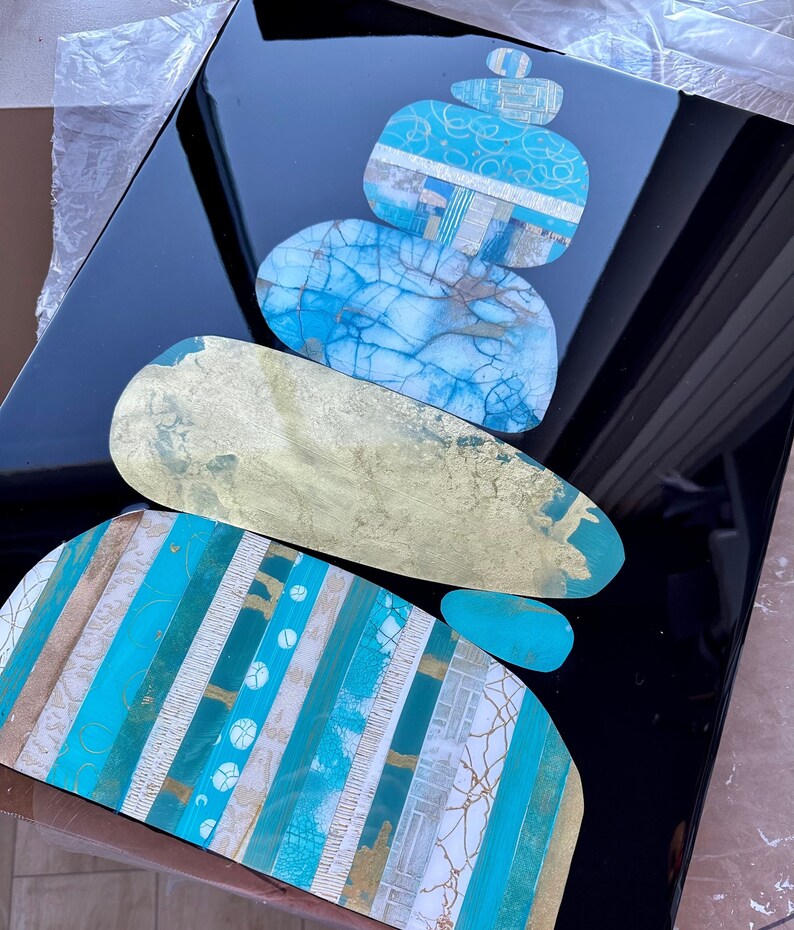 Puede incluir: Una pila de piedras abstractas de forma org&aacute;nica en tonos de azul, blanco y dorado, dispuestas en una formaci&oacute;n zen sobre un fondo negro.