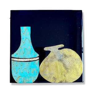 Puede incluir: Un jarr&oacute;n azul turquesa con un patr&oacute;n ondulado y una banda dorada se encuentra junto a un objeto redondo texturizado dorado y blanco sobre un fondo negro.