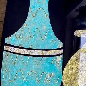 Puede incluir: Un jarr&oacute;n azul turquesa con un patr&oacute;n ondulado dorado y una banda dorada alrededor del centro. El jarr&oacute;n est&aacute; sobre un fondo negro.