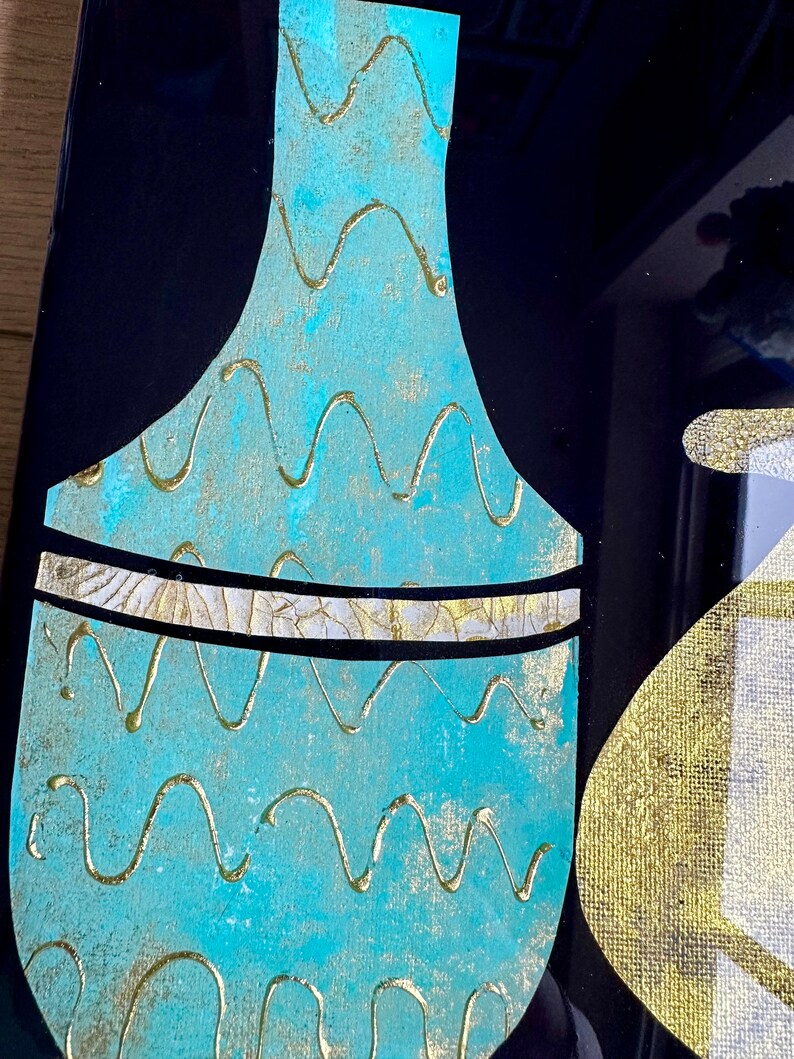 Puede incluir: Un jarr&oacute;n azul turquesa con un patr&oacute;n ondulado dorado y una banda dorada alrededor del centro. El jarr&oacute;n est&aacute; sobre un fondo negro.