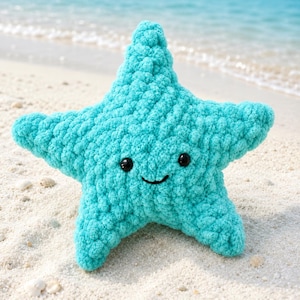 Puede incluir: Un peluche de estrella de mar turquesa, tejido a ganchillo, con ojos de seguridad negros y una boca sonriente. El peluche está hecho de un hilo suave y texturizado, sobre una playa de arena.