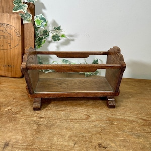 May include: A small, vintage wooden display shelf with a rectangular shape. The shelf has a dark brown finish and features decorative cutouts on the sides. It is designed to hold small items and is elevated on short legs.
