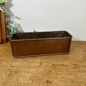 May include: A rectangular metal container with a weathered, rusted brown finish. The vessel features a deep, open interior with visible signs of oxidation and wear on the exterior surfaces, including a thin, metallic rim along the base edge.