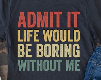 May include: A navy blue t-shirt with the text "ADMIT IT LIFE WOULD BE BORING WITHOUT ME" in red, yellow, and green. The shirt is paired with blue jeans and white canvas sneakers.