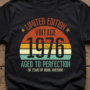 Peut inclure: T-shirt noir avec un motif vintage. Le motif présente le texte "LIMITED EDITION VINTAGE 1976 AGED TO PERFECTION - 50 YEARS OF BEING AWESOME -" dans un style rétro avec des couleurs orange, jaune et turquoise.