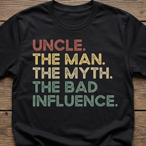 May include: Black t-shirt with the text "UNCLE. THE MAN. THE MYTH. THE BAD INFLUENCE." in a retro font. The text is in red, yellow, and green colors. The shirt is made of a soft material.