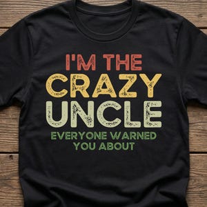 May include: Black t-shirt with the text "I'M THE CRAZY UNCLE EVERYONE WARNED YOU ABOUT" in a retro font. The text is in shades of red, yellow, and green. The shirt is made of a soft material.