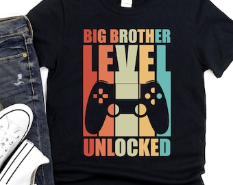 Puede incluir: Camiseta negra con un gráfico de mando de videojuego de estilo retro y el texto "Big Brother Level Unlocked".