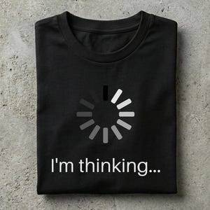 Może przedstawiać: Czarny t-shirt z okrągłym dekoltem, ozdobiony białym, okrągłym symbolem ładowania umieszczonym na środku klatki piersiowej. Poniżej ikony znajduje się napis "I'm thinking..." wykonany wyraźną, białą czcionką bezszeryfową. Koszulka jest starannie złożona.