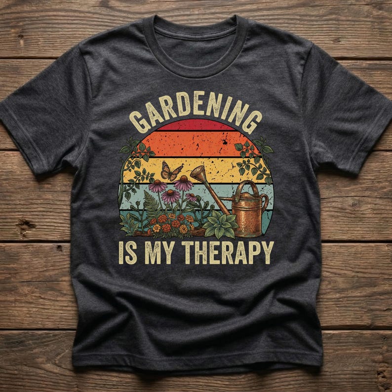 May include: Dark gray t-shirt featuring a colorful graphic with the text "Gardening is My Therapy." The design includes a sunset, flowers, a butterfly, and a watering can, perfect for gardening enthusiasts.