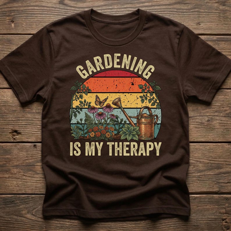 May include: Brown t-shirt with a colorful graphic. The graphic features a sunset design with the words "Gardening is my Therapy" in white. The design includes flowers, a watering can, and a butterfly.