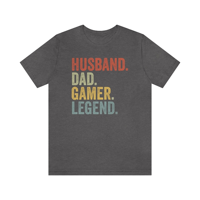 May include: Dark gray t-shirt with a vintage-style graphic that reads "Husband. Dad. Gamer. Legend."