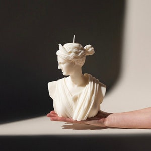 May include: A white sculpted candle in the shape of a woman's bust. The candle has a detailed design and is a decorative piece.