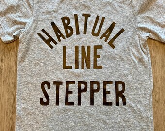 May include: A gray t-shirt with black text that reads "Habitual Line Stepper".