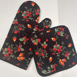 Puede incluir: Juego de manopla y salvamanteles negros con un estampado de fresas y frambuesas rojas con hojas verdes. Los textiles de cocina están acolchados y tienen un borde negro.