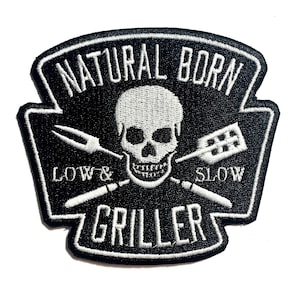 May include: Black and white embroidered patch with the text "NATURAL BORN GRILLER" and a skull graphic. The patch also features crossed grilling tools and the words "LOW & SLOW".