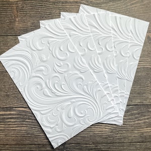 May include: Five white embossed cardstock sheets with a swirling, floral pattern. The sheets are stacked on top of each other.