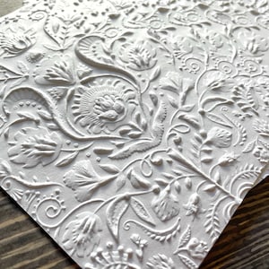 May include: A stack of white embossed paper cards with a floral pattern. The cards have a raised, textured design.