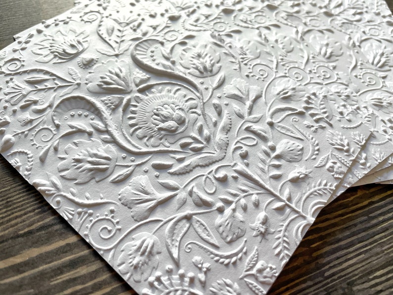 May include: A stack of white embossed paper cards with a floral pattern. The cards have a raised, textured design.