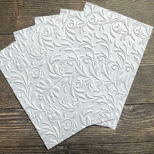 May include: Four sheets of white embossed paper with a floral pattern. The paper has a raised, textured design.