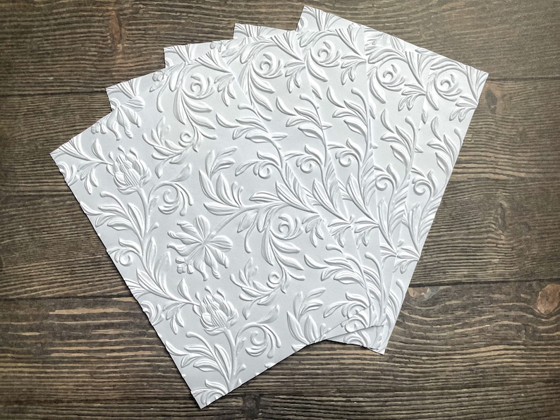 May include: Four sheets of white embossed paper with a floral pattern. The paper has a raised, textured design.