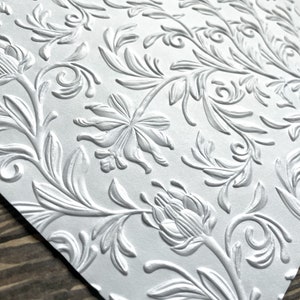 May include: White embossed paper with a repeating floral pattern. The design features stylized flowers and leaves.
