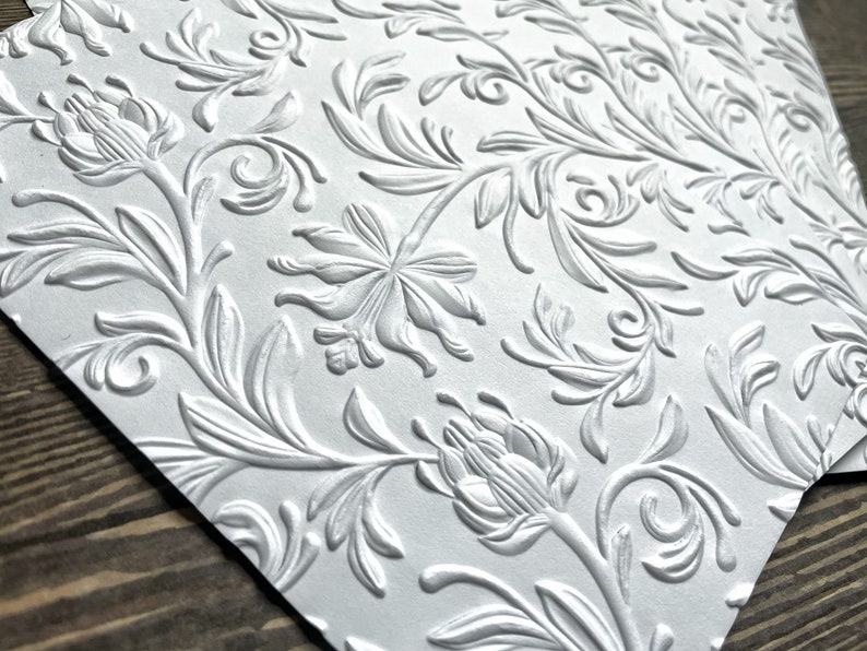 May include: White embossed paper with a repeating floral pattern. The design features stylized flowers and leaves.