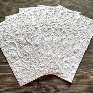 May include: Five white embossed paper cards with a floral pattern. The cards are stacked on top of each other.