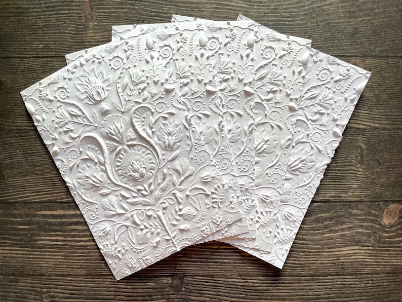 May include: Five white embossed paper cards with a floral pattern. The cards are stacked on top of each other.