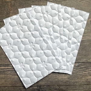 May include: Five white cardstock sheets with an embossed pattern of overlapping circles and teardrop shapes.